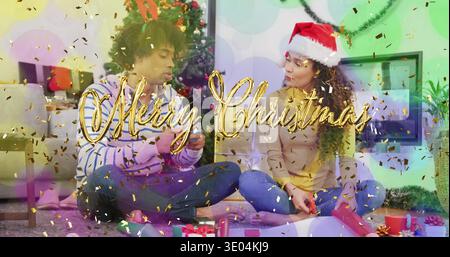 Wrapping couple sitting on carpet in home, woman wearing Santa hat, with decorated tree and gifts Stock Photo