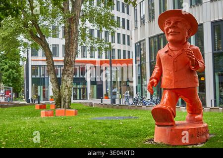 A vibrant orange statue of a walking man wearing a hat and suit stands prominently on a grassy urban plaza in Frankfurt, Germany. The contemporary... Stock Photo