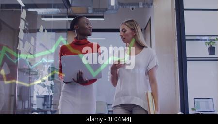 Walking two colleagues in red, white, discussing work in office hall with laptop and glass graphs Stock Photo