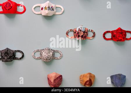 A collection of colorful, artistic face masks displayed on a light blue wall in a grid arrangement. The masks feature various designs including... Stock Photo