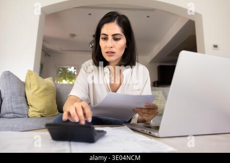 Serious young Latin woman calculating domestic budget at home Stock Photo