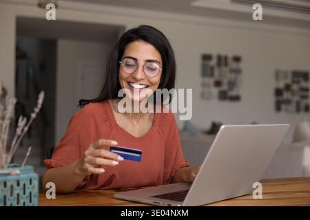 Smiling Brazilian woman in glasses enjoy online shopping at home Stock Photo