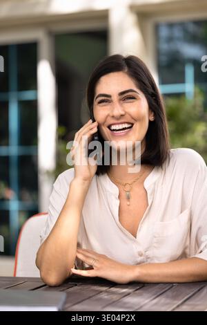 Cheerful young Hispanic freelancer woman talking on mobile phone Stock Photo