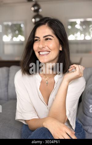 Happy attractive young Hispanic woman sitting on comfortable couch Stock Photo