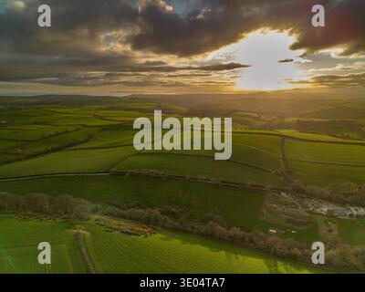 Aerial drone photograph of sunset light over patchwork farmland fields and rolling countryside landscape near Looe in Cornwall, England. Stock Photo