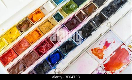 Open plastic box of professional watercolor paints on a white background. Close-up of a used watercolor paint collection. Art supplies, creativity con Stock Photo
