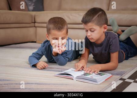 two brothers are lying on the floor reading a book Stock Photo