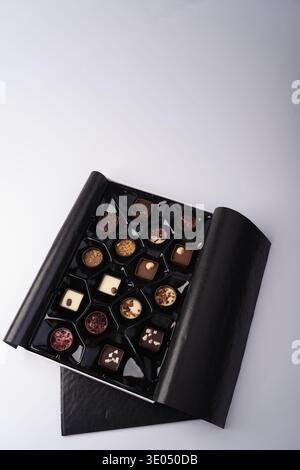 open luxury black box of assorted artisanal chocolates and pralines arranged in a glossy black tray on a pale studio tabletop, refined minimal present Stock Photo