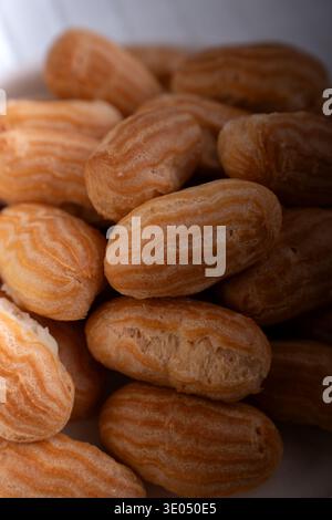 close-up of piled golden-brown choux pastry shells (mini éclairs) with ridged textured surfaces, warm soft lighting and shallow depth-of-field evoking Stock Photo