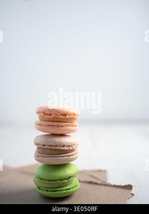 three pastel macarons stacked on torn brown paper on a light wooden tabletop with a soft pale-blue minimal background, highlighting delicate shells, c Stock Photo