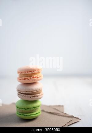 stack of three pastel macarons (peach, beige, green) delicately balanced on torn kraft paper against a bright minimalist white tabletop background, so Stock Photo