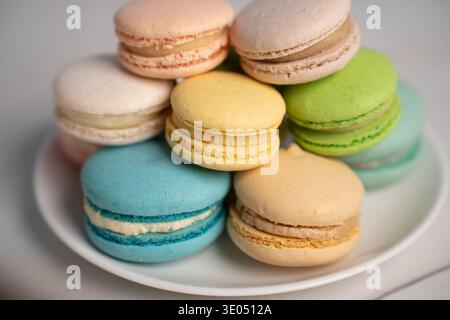 studio close-up of a stacked assortment of pastel french macarons on a white plate set on a neutral tabletop, showcasing delicate crisp shells, creamy Stock Photo