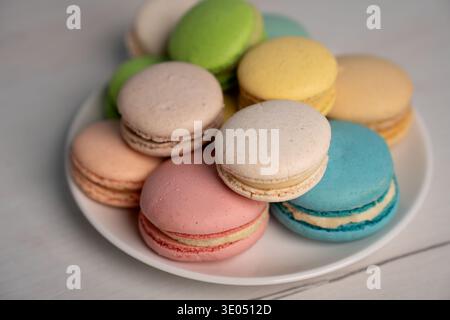 close-up of a pile of colorful pastel french macarons arranged on a white plate on a light wooden tabletop, bathed in soft natural light that highligh Stock Photo