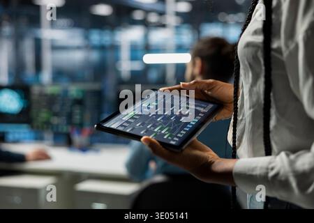 Close up of programmer in data center using tablet, managing AI training datasets. IT employee using device to oversee machine learning in server farm supporting scalable infrastructure for AI apps Stock Photo