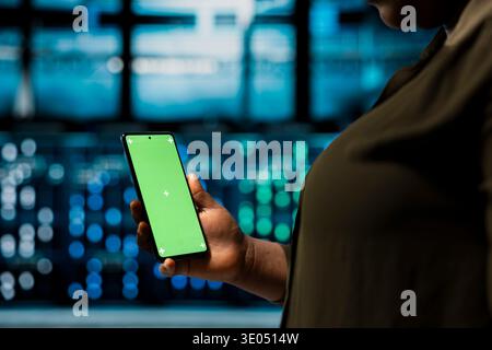 Close up of data center admin monitoring hardware parts for potential failures using green screen smartphone. Server hub worker uses mockup mobile phone to configure settings, increasing uptime Stock Photo