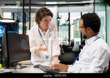 Manager overseeing admin using computer in workplace to do maintenance on neural networks. Team leader supervising IT expert in tech startup office using AI machine learning systems on PC Stock Photo