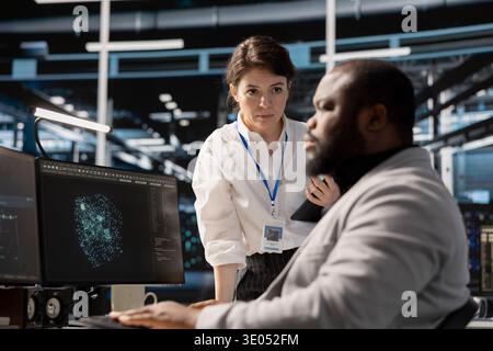 Manager supervising engineer in data center managing server virtualization, running scripts. Team leader overseeing work done by employee using programming language in server farm Stock Photo