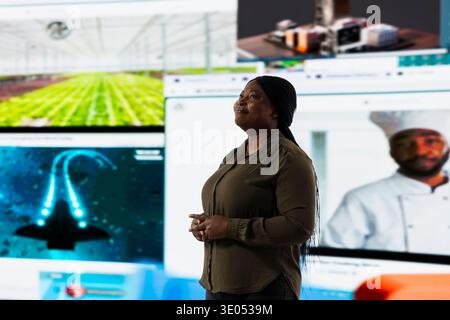 Smiling woman looking at digital videowall, enjoying endless entertainment selection. Happy person pleased by access to various streaming options, looking at screens displaying movies and TV shows Stock Photo