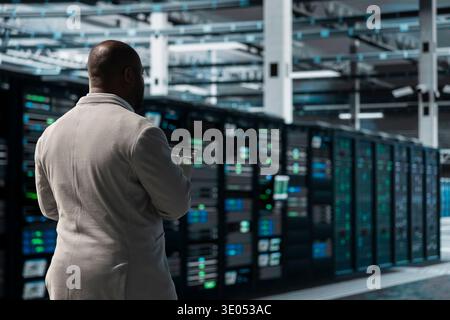 Developer in data center coding on laptop, troubleshooting backend operations. Server room IT expert using programming scripts on laptop, maintaining operational reliability Stock Photo