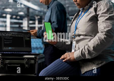 Server farm worker reading notifications on mockup phone while resting between tasks. Close up of data center admin using green screen smartphone to relax, waiting for programming software to run Stock Photo