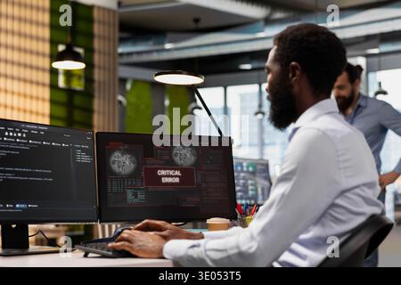 Engineer resolving critical error alert on screen in tech startup office, troubleshooting system warnings. IT professional addressing critical failure message, debugging office equipment Stock Photo
