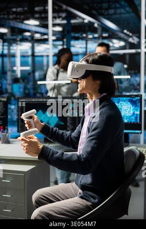 Developer wearing VR headset coding in data center, updating AI automation scripts. Server room employee using virtual reality, programming artificial intelligence algorithms Stock Photo