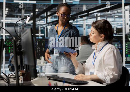 Technicians in data center reviewing clipboard, evaluating infrastructure maintenance tasks notes. Engineering team conducting check on systems, assessing progress on maintenance goals Stock Photo