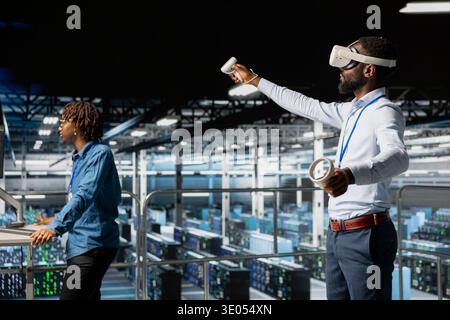 African american IT programmer uses virtual reality tech on industrial platform, collaborating on automation tasks. Server hub engineer visualizing large language model infrastructure with VR. Stock Photo