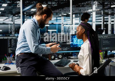 Manager and intern in data center installing upgraded server racks systems helped by AI. Server room team leader and worker doing brainstorming, upgrading gear using artificial intelligence Stock Photo