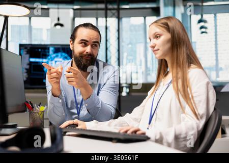 Senior programmer guiding junior developer through AI tool integration, mentoring her on using machine learning APIs. Lead developer teaching intern to use artificial intelligence Stock Photo