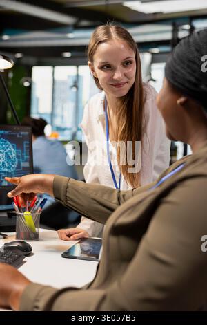Pleased manager mentoring junior dev at desk in office, congratulating her for optimizing AI code. Satisfied tech startup IT specialist offering positive feedback to female developer intern Stock Photo
