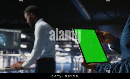 Close up of server hub admin using isolated screen tablet next to colleague reviewing AI LLM visualization. Data center employee using mockup device to monitor machine learning systems, Stock Photo