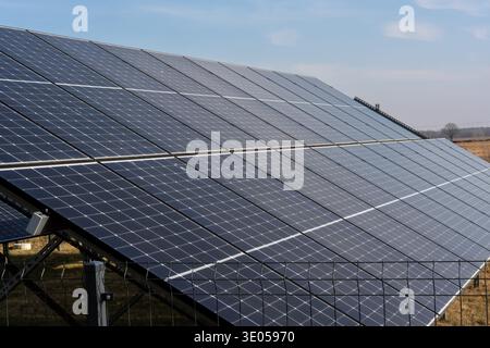 Close-up of large industrial solar photovoltaic panel array with blue cells and metal frame against clear sky in rural area.  Stock Photo