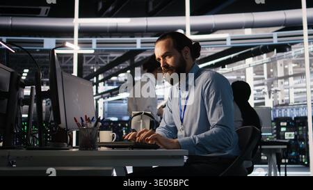Server room IT specialist frustrated by difficult complex tasks in office. Stressed engineer developing neural network software while working extended hours in data center, camera A Stock Photo