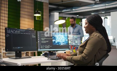 Female technician using computer to write code, developing machine learning APIs. African american woman troubleshooting software errors and faults using artificial intelligence, camera A Stock Photo