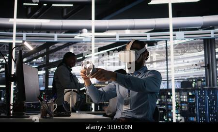 Data center employee wearing VR headset using artificial intelligence neural networks technology. Server farm programmer using AI programming language and virtual reality to update hardware, camera A Stock Photo