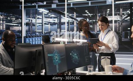 Data center teamworking colleagues performing maintenance on server racks used for artificial intelligence processing. Engineering team managing server hub rigs used for machine learning, camera A Stock Photo