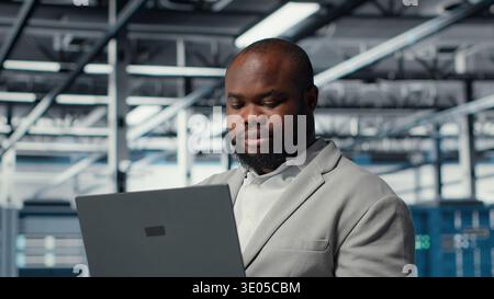 Close up of engineer in server room using laptop, executing security patches, verifying firewall configurations. Worker performing equipment vulnerability scans in data center, camera B Stock Photo