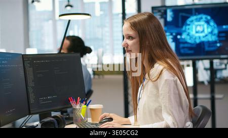 Young female programmer using computer to write code, developing machine learning APIs. Junior developer troubleshooting software errors and faults using artificial intelligence, camera A Stock Photo