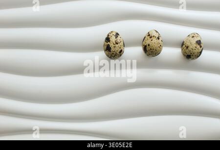 Minimal Easter composition with three quail eggs placed on modern wavy white surface. Clean seasonal background with large copy space. Stock Photo