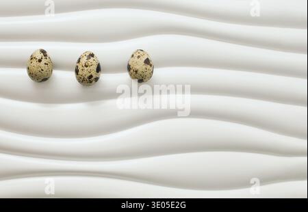 Minimal Easter composition with three quail eggs placed on modern wavy white surface. Clean seasonal background with large copy space. Stock Photo