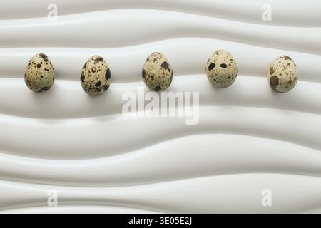 Row of quail eggs arranged on modern wavy white surface. Minimal Easter background with natural texture and clean composition. Stock Photo