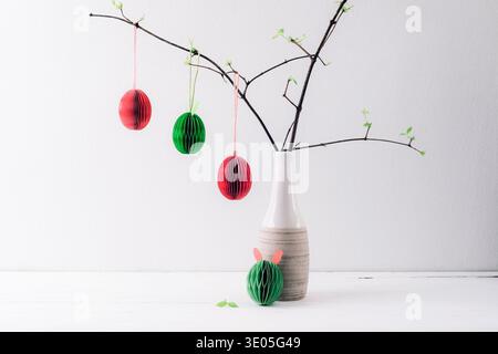 Paper Easter eggs hanging on branches in vase on white background. Still life, Easter holiday decorations. Stock Photo