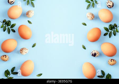 Brown Easter eggs and quail eggs with green leaves on light blue background. Top view, flat lay, copy space. Stock Photo