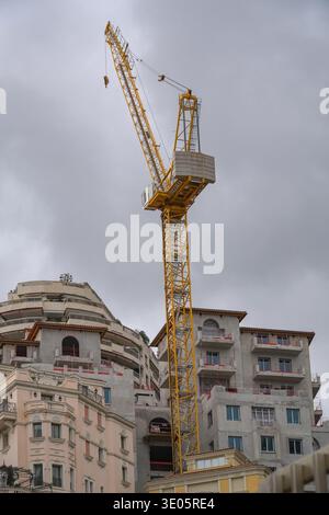 Tower crane dominating residential construction, Monaco, French Riviera. High-density urban development against overcast sky. Stock Photo