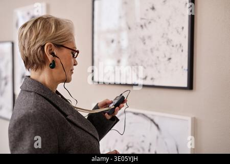 Senior Caucasian Woman Engaging with Audio Guide While Exploring Modern Artworks Stock Photo