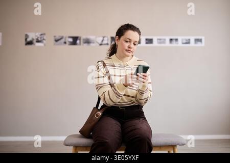 Young Adult Caucasian Woman Sitting Indoors Using Smartphone While Waiting Stock Photo