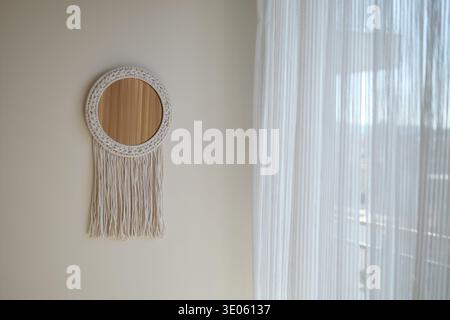 Decorative mirror hangs on wall near white curtain Stock Photo