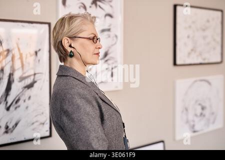 Senior Caucasian Woman Observing Abstract Artworks in Modern Gallery Stock Photo