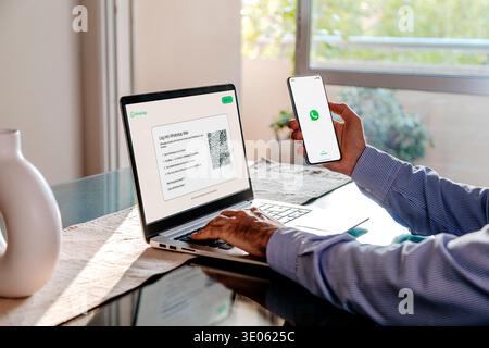Man using smartphone to log into WhatsApp Web on laptop at home, mobile messaging and digital communication concep Stock Photo